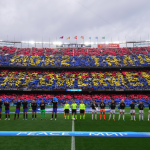 Players of FC Barcelona and Real Madrid line up as fans perform a tifo in the stands 